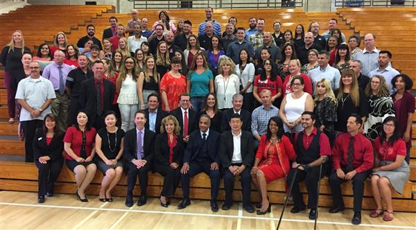 A large group of adults sit and stand on gym bleachers